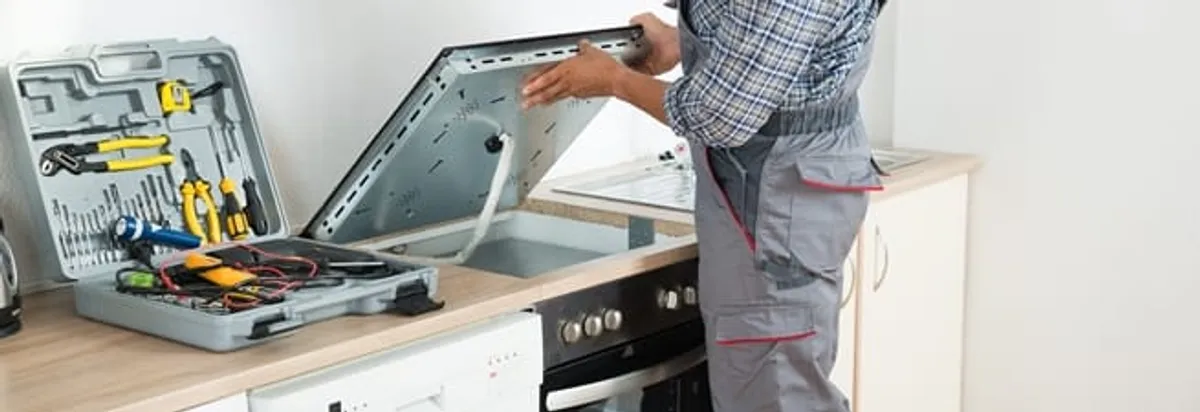 Cooktop repair technician lifting a built-in stovetop for service in Des Moines, IA