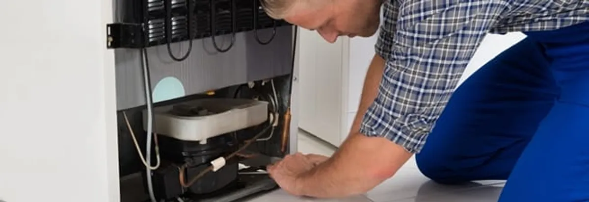 Refrigerator repair technician servicing the compressor and condenser area in Des Moines, IA